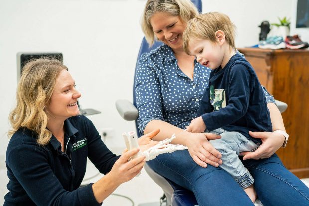 Chelsea Holding Baby's Foot While Sitting On Mothers Lap In Podiatry Chair — Podiatrists in Alice Springs, NT